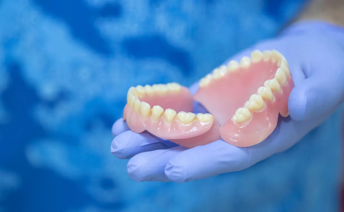 Dentures held in gloved hand; pink and white plastic teeth.